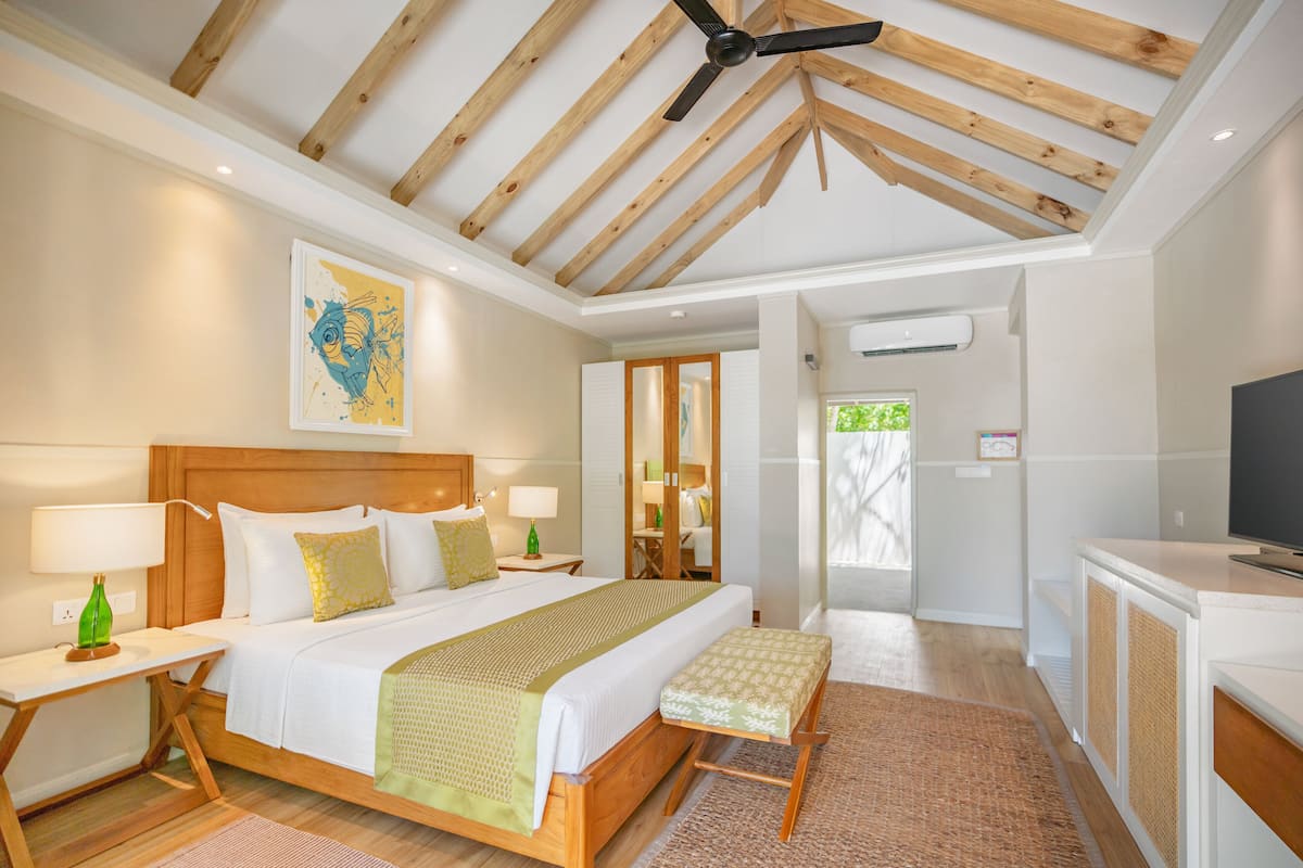 A spacious bedroom with a large bed, wooden ceiling beams, a ceiling fan, and a television on a cabinet.