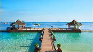 A wooden pier leading to overwater bungalows with clear blue water and a small boat in the distance. - Ellaidhoo Maldives by Cinnamon (Ellaidhoo)