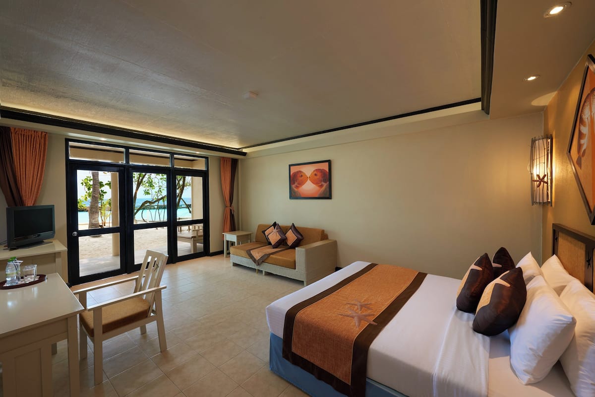 A hotel room with a bed, a desk, a chair, a television, and a large window with a view of the beach.