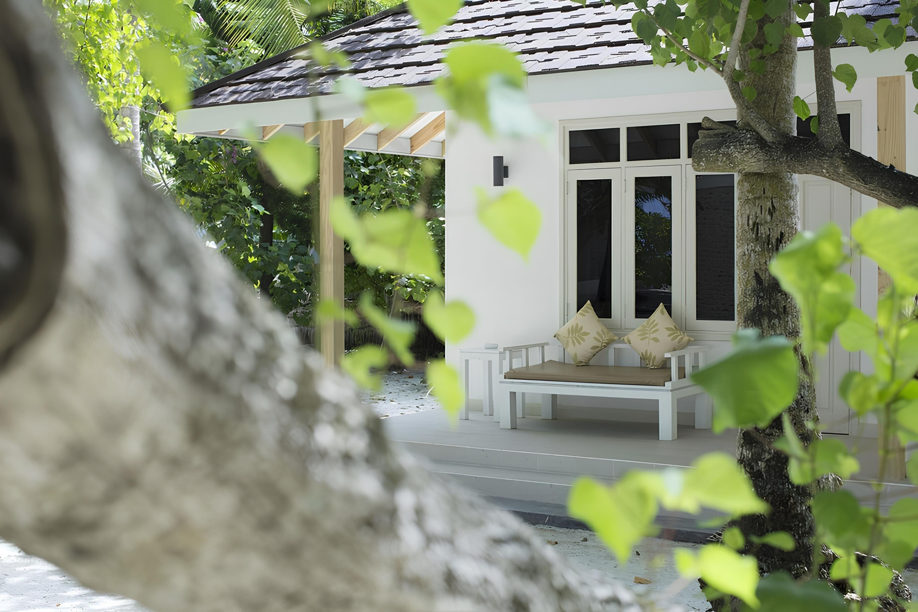 A white building with a porch and a bench.