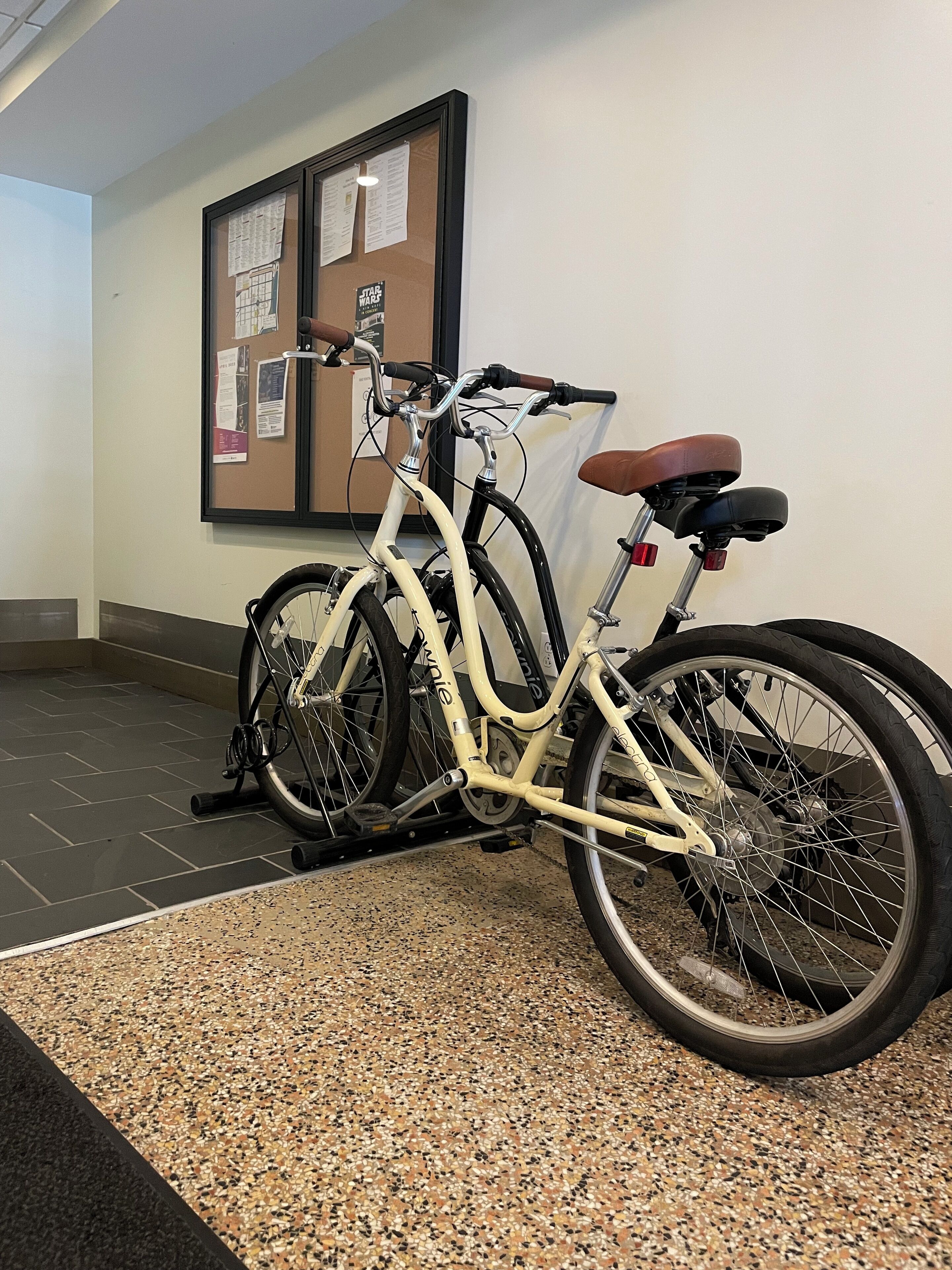 Un vélo est garé à l’intérieur, et un panneau d’affichage en liège est accroché au mur derrière lui.