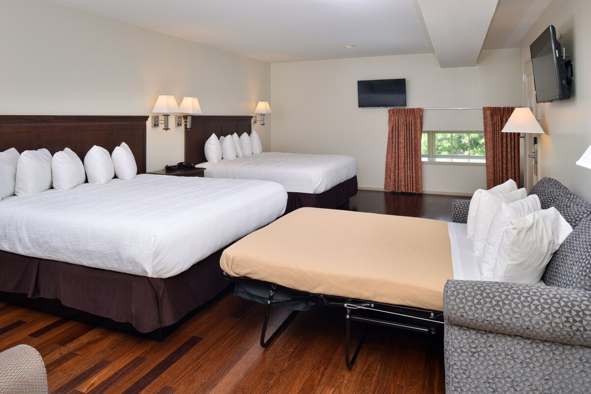 A hotel room with two beds, a sofa, a TV, and a window with curtains.