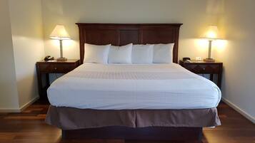Una cama bien hecha con sábanas blancas y un cabecero de madera, flanqueada por dos mesitas de noche con lámparas, en una habitación con suelo de madera.