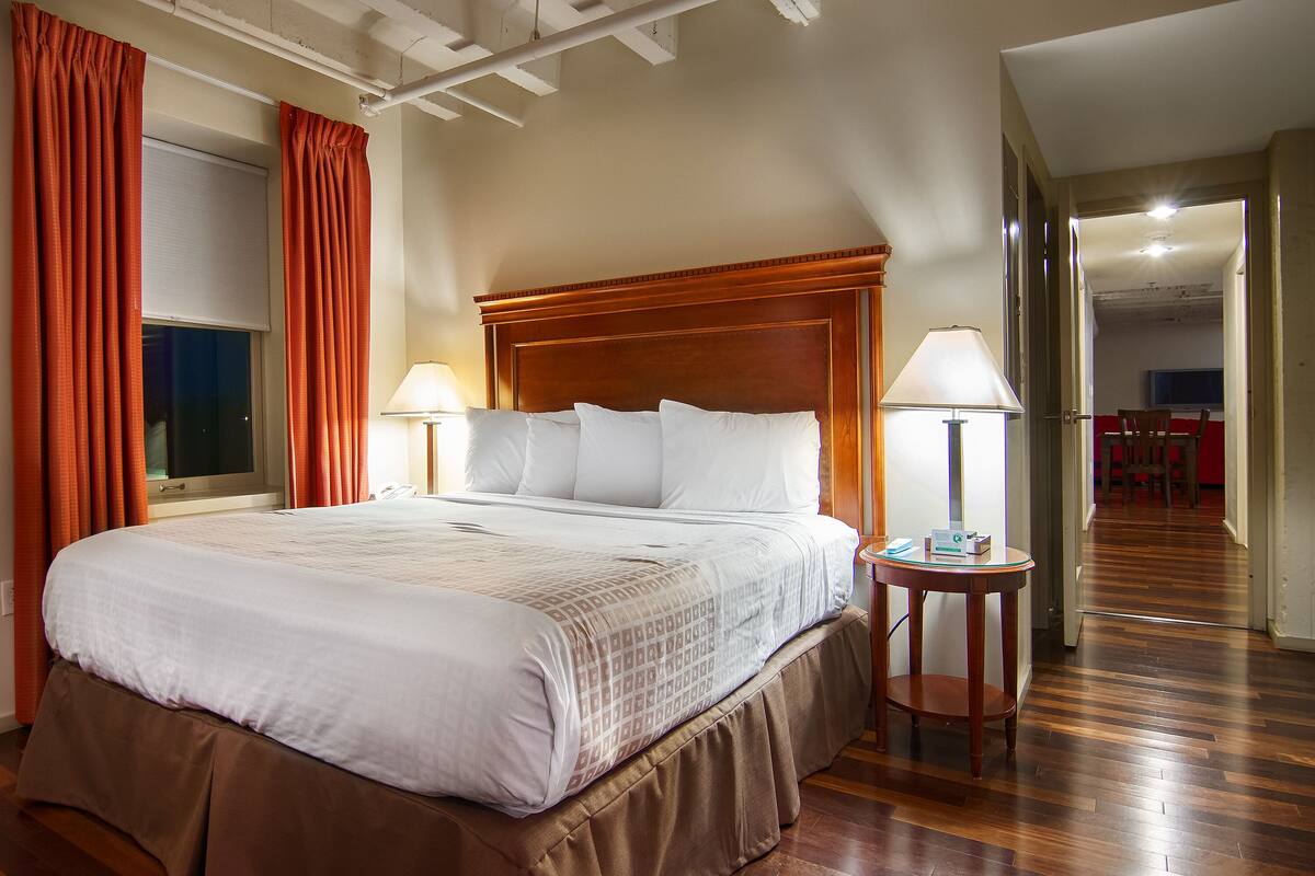A hotel room with a large bed, two bedside lamps, a wooden headboard, and a window with curtains.