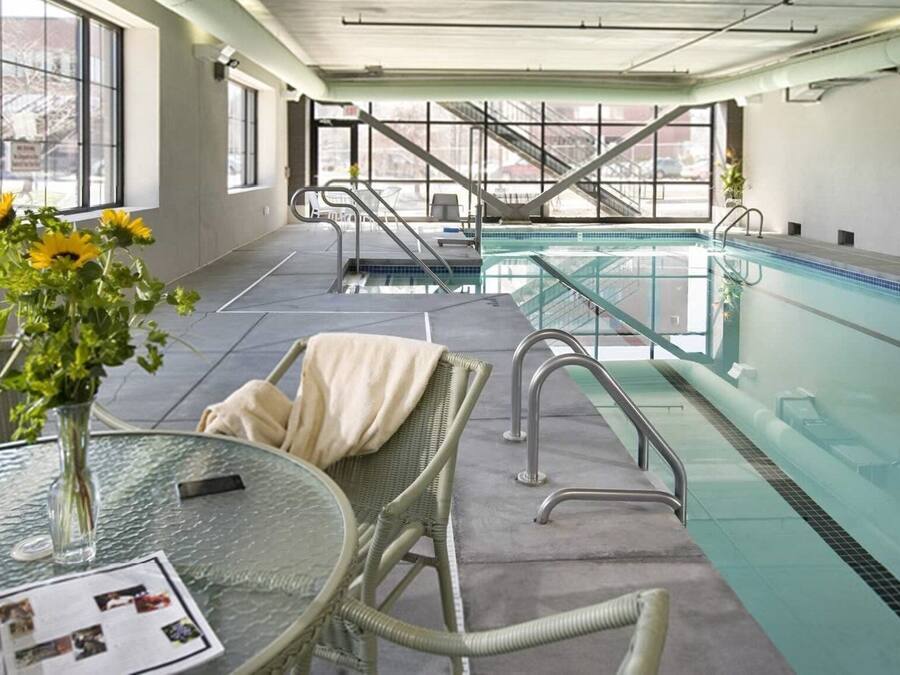 An indoor swimming pool area with a glass table, wicker chairs, and a vase of flowers.