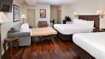 A hotel room with two beds, a sofa, a small table, and a desk.