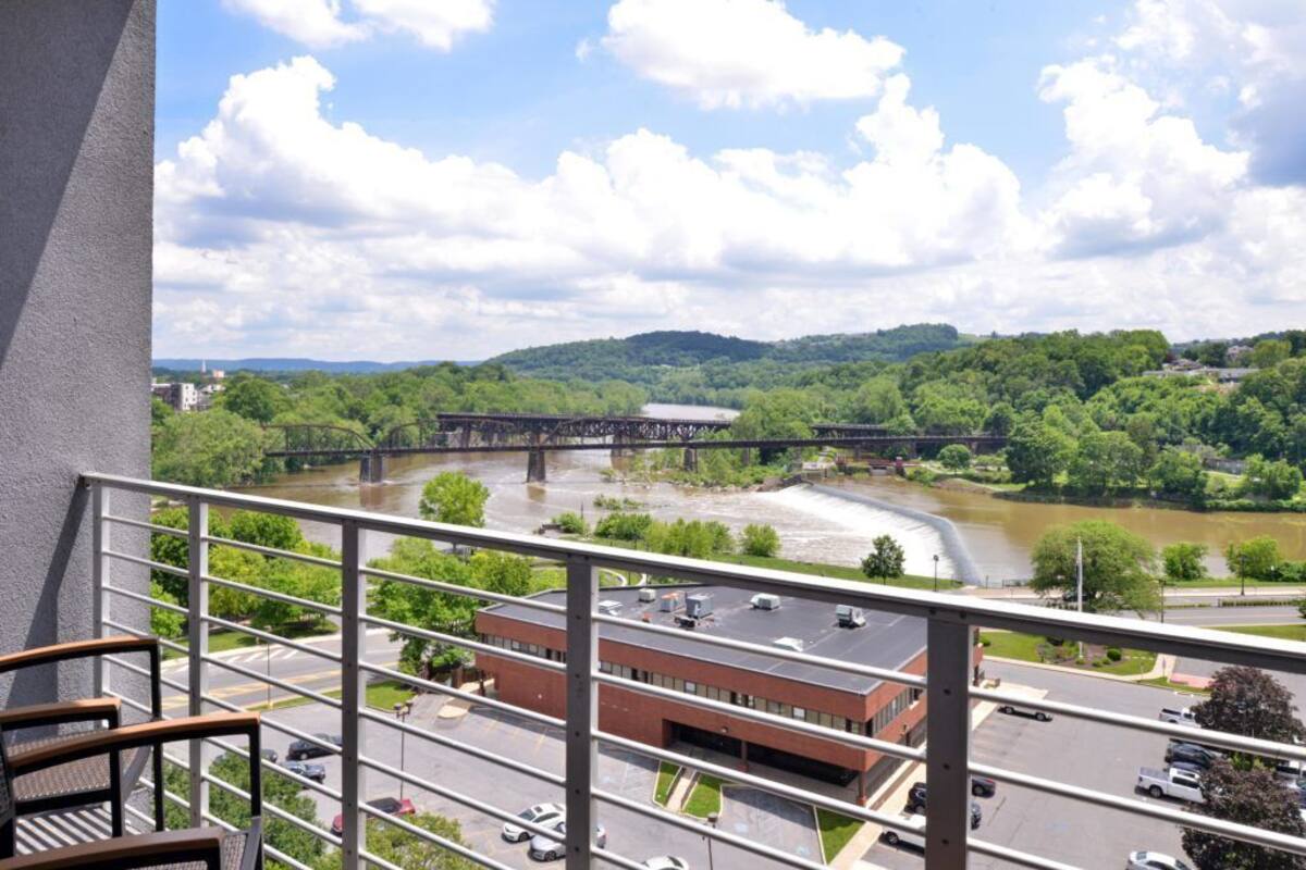 A view from a balcony overlooking a river, a bridge, and a building with a parking lot.