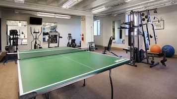 A gym with a ping pong table, exercise equipment, and a mirror.