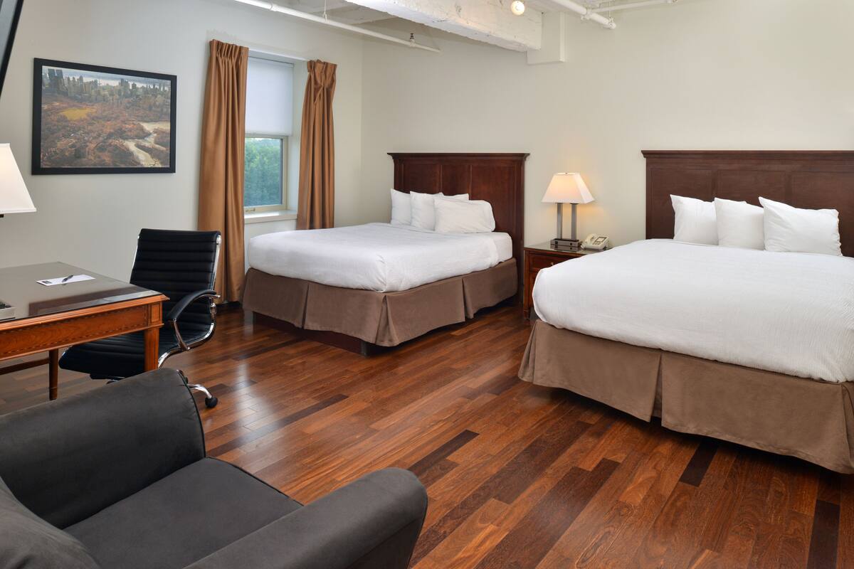 A hotel room with two beds, a desk, a chair, and a window with curtains.