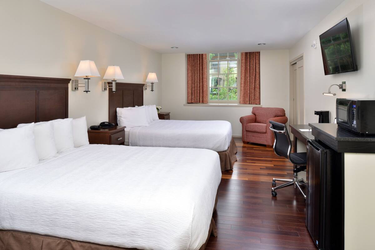 A hotel room with two beds, a desk with a computer, a TV, and a chair.