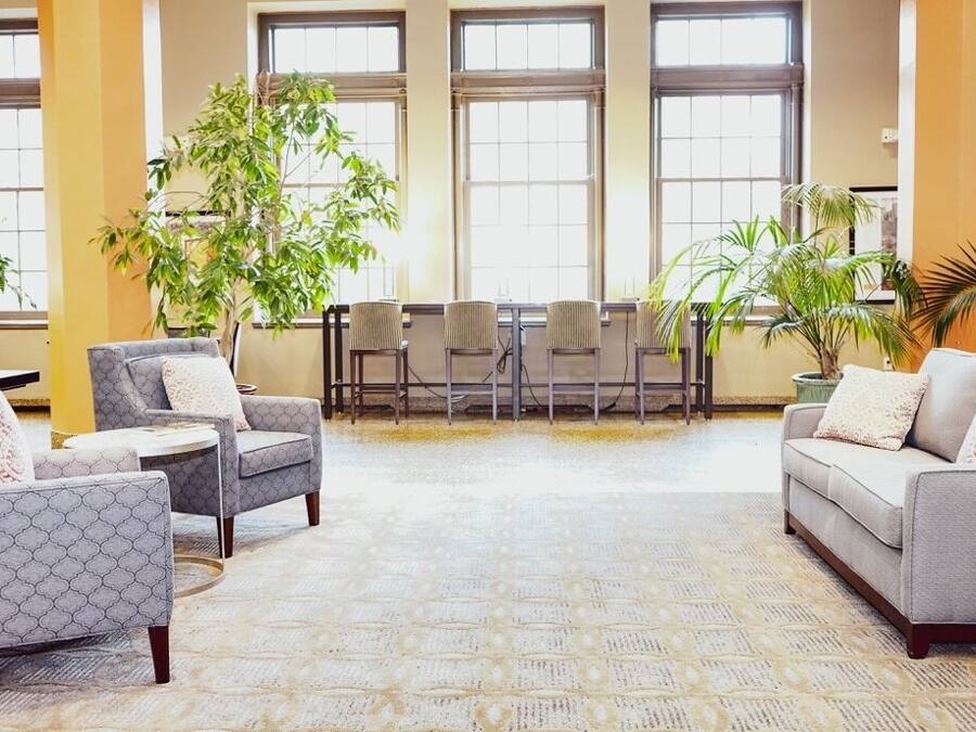 Un vestíbulo amplio con techo alto, ventanas grandes y diversas opciones de asientos, incluyendo sofás y sillones.