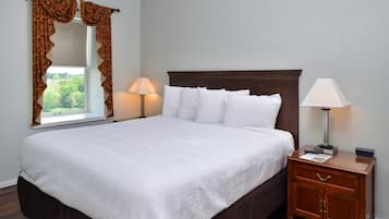 A neatly made bed with white linens, a wooden nightstand with a lamp, and a window with curtains.