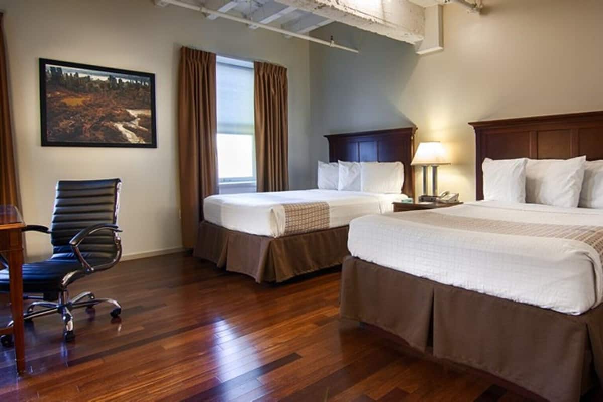 A hotel room with two beds, a desk, a chair, and a painting on the wall.