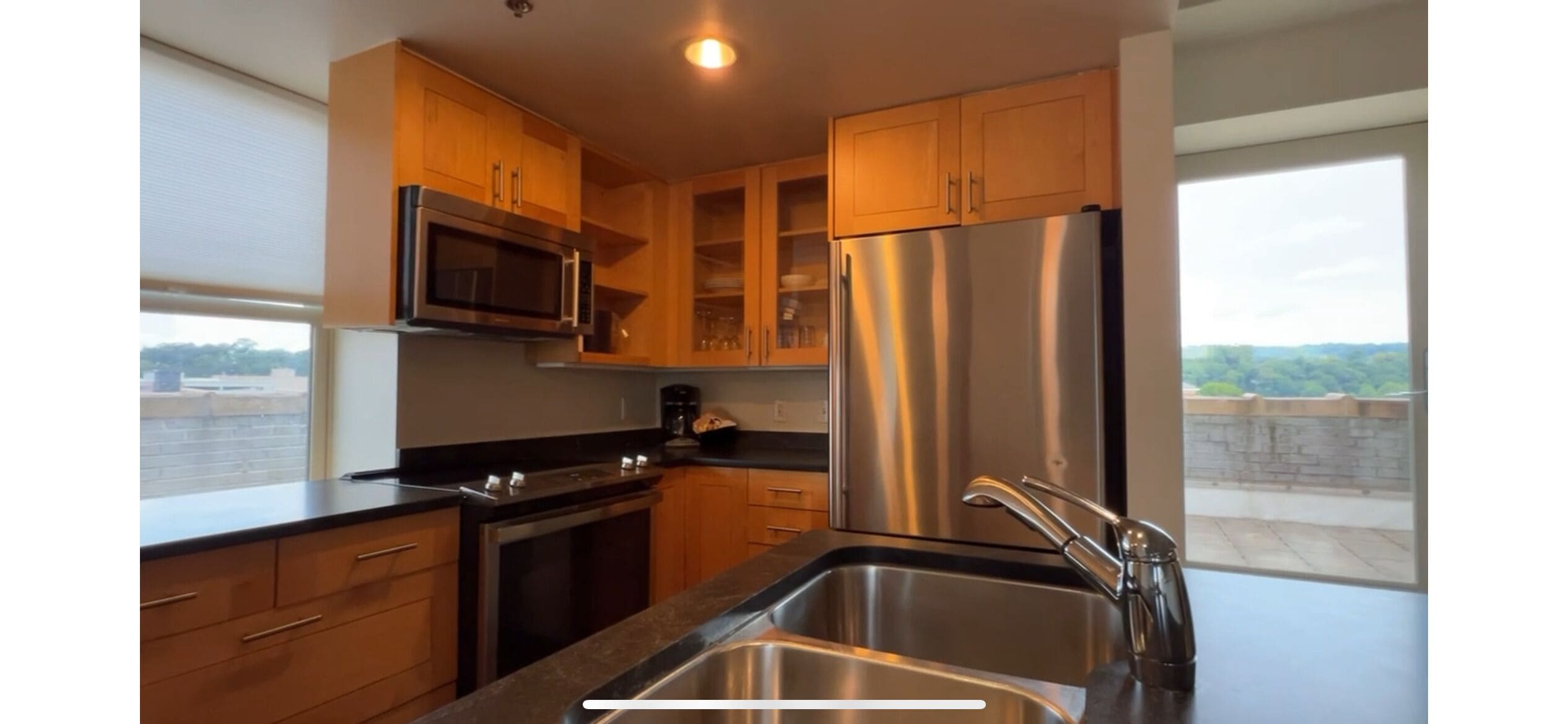 A modern kitchen with stainless steel appliances, wooden cabinets, and a large window offering a view of the cityscape.
