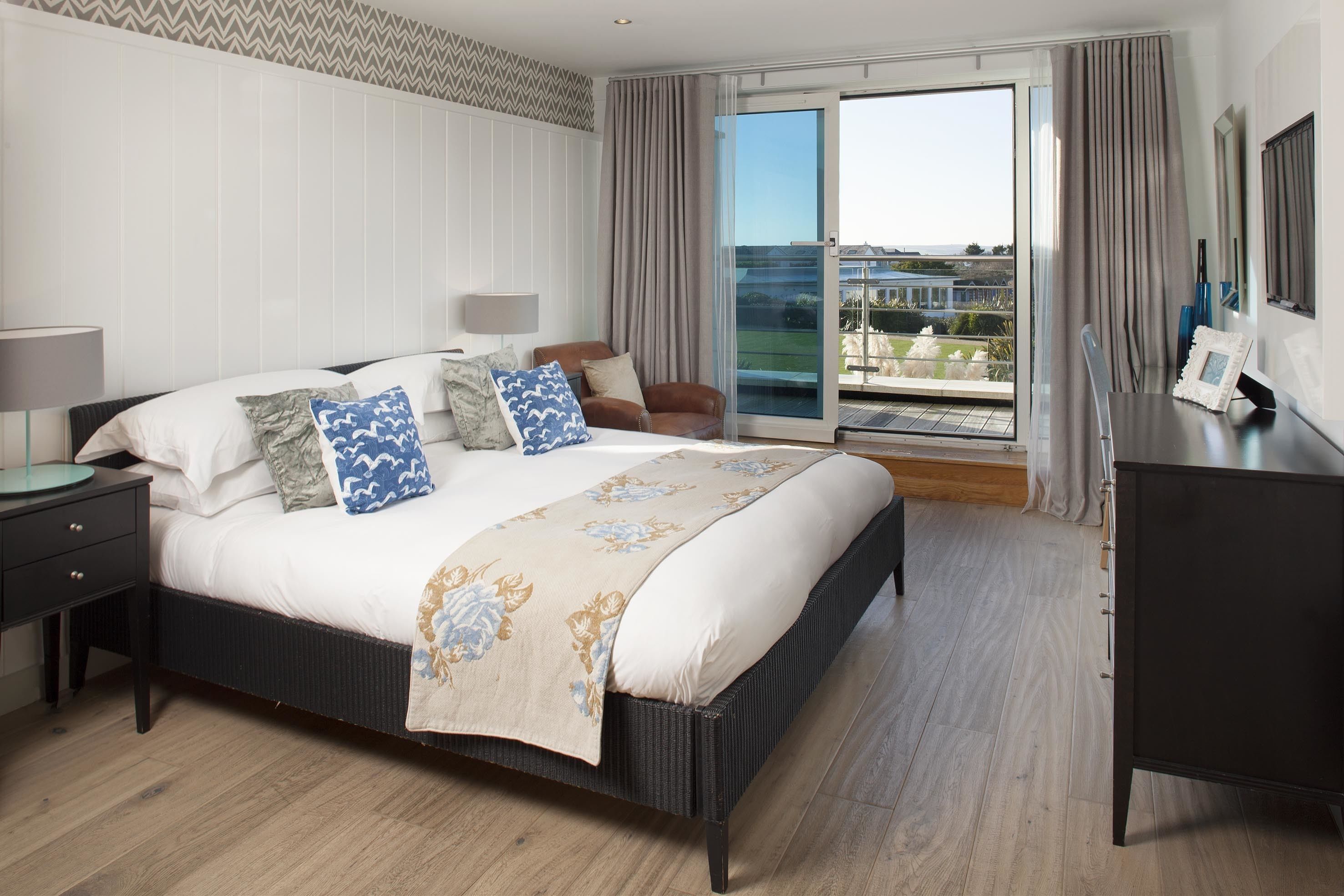Un dormitorio con una cama grande, una mesita de noche, una silla, un escritorio y vistas al exterior a través de una puerta corredera.