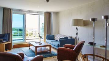 A modern hotel room with a balcony, a sofa, a coffee table, and leather chairs.