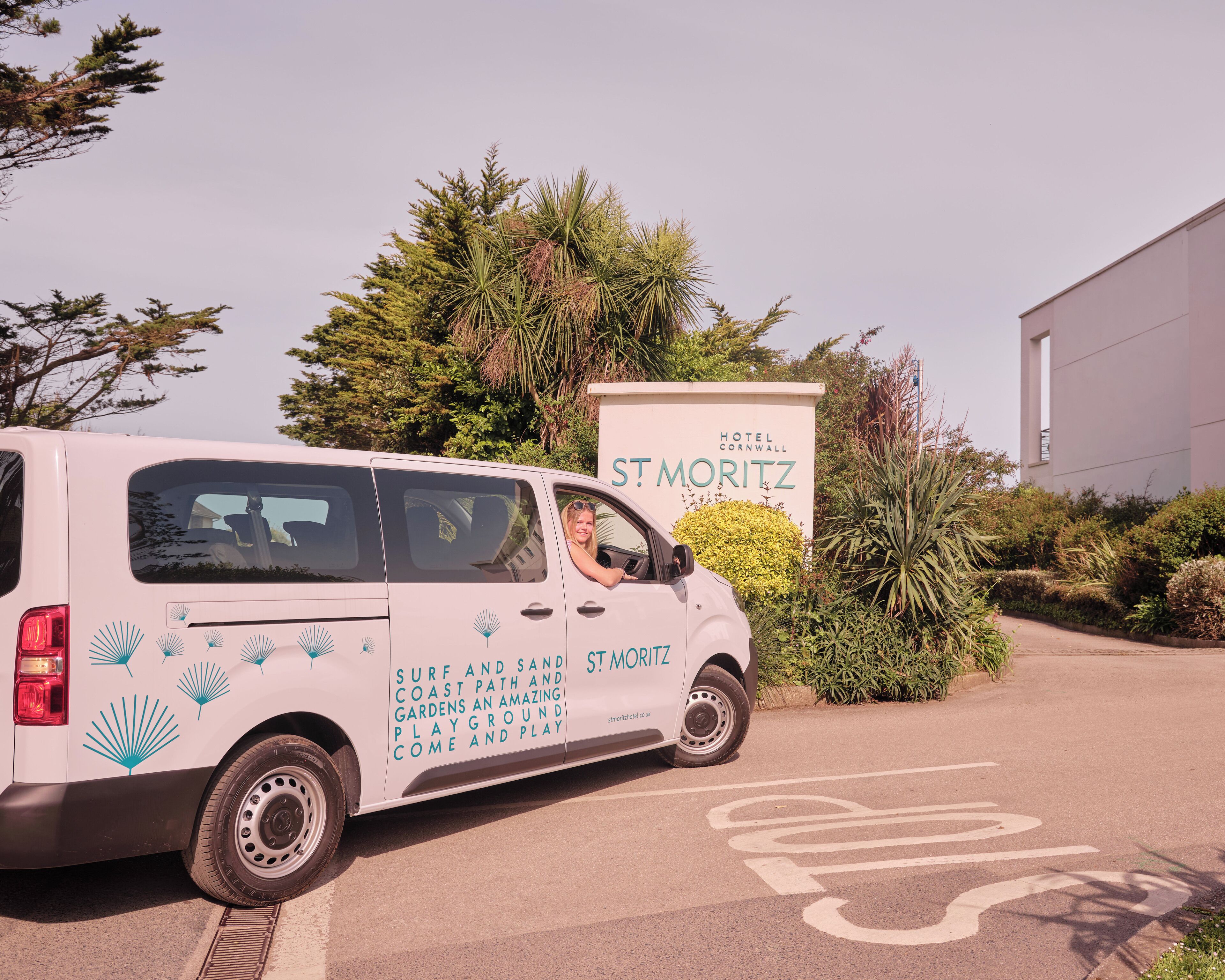 A white van parked in front of a hotel named "St. Moritz" with a sign advertising "Surf and Sand Coast Path and Gardens".