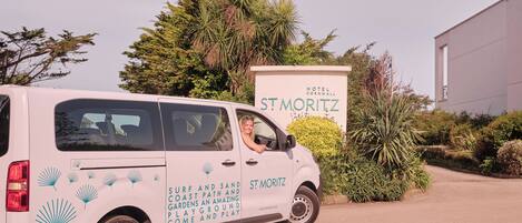 A white van parked in front of a hotel named "St. Moritz" with a sign advertising "Surf and Sand Coast Path and Gardens".