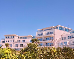 Un hotel de varios pisos con balcones y ventanas amplias, rodeado de vegetación tropical.