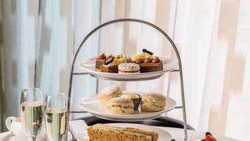 Un soporte de tres niveles con diversos pasteles y sándwiches, acompañado de copas de champán y tazas de té.