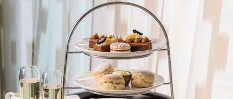 A three-tiered dessert stand with various pastries and sandwiches, accompanied by glasses of champagne and cups of tea.