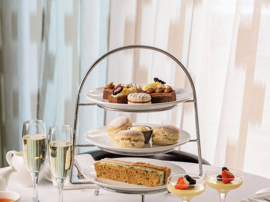 A three-tiered dessert stand with various pastries and sandwiches, accompanied by glasses of champagne and cups of tea.