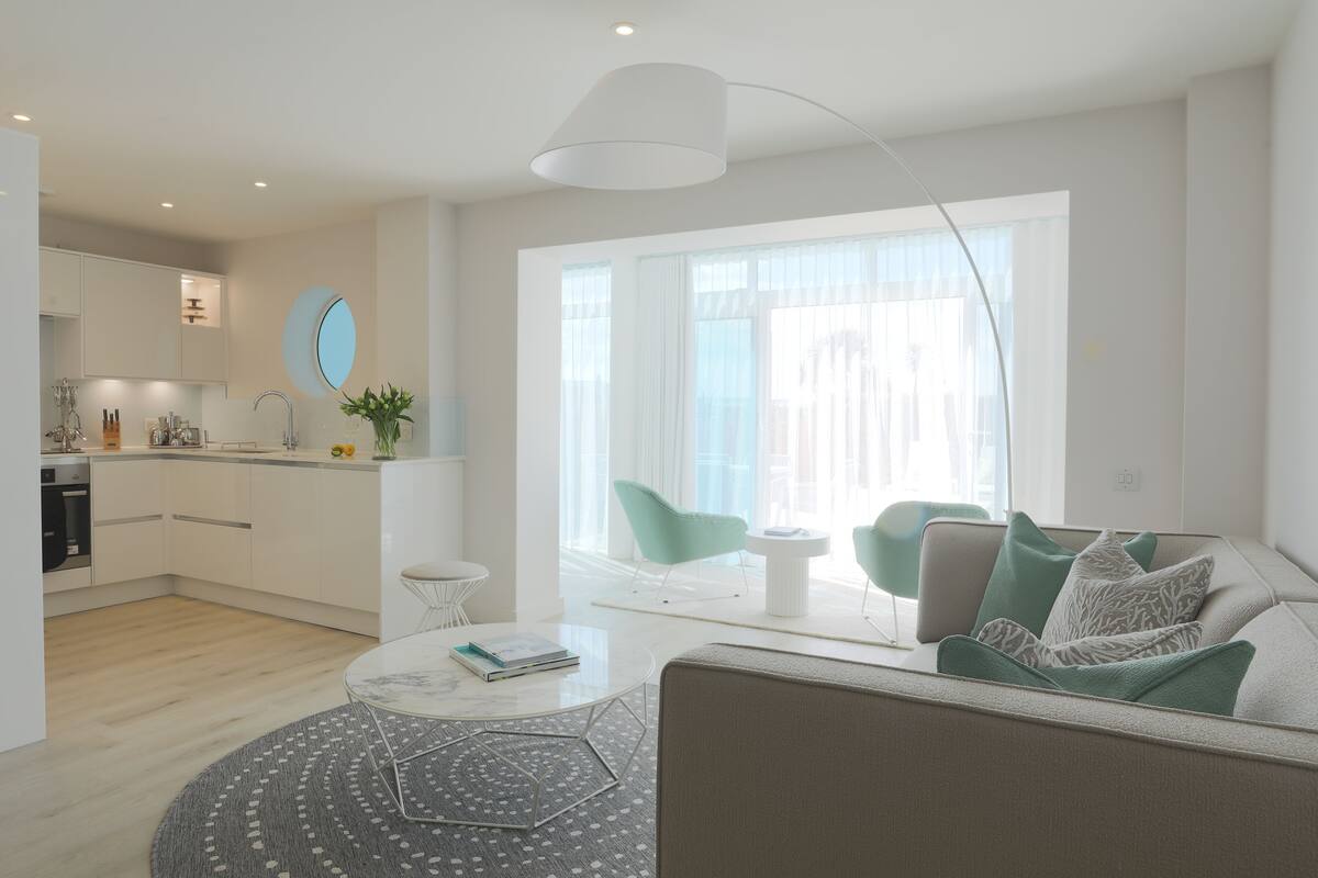 Una sala de estar moderna con sofá, mesa de centro y comedor, con una cocina al fondo.