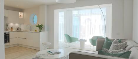 Una sala de estar moderna con sofá, mesa de centro y comedor, con una cocina al fondo.