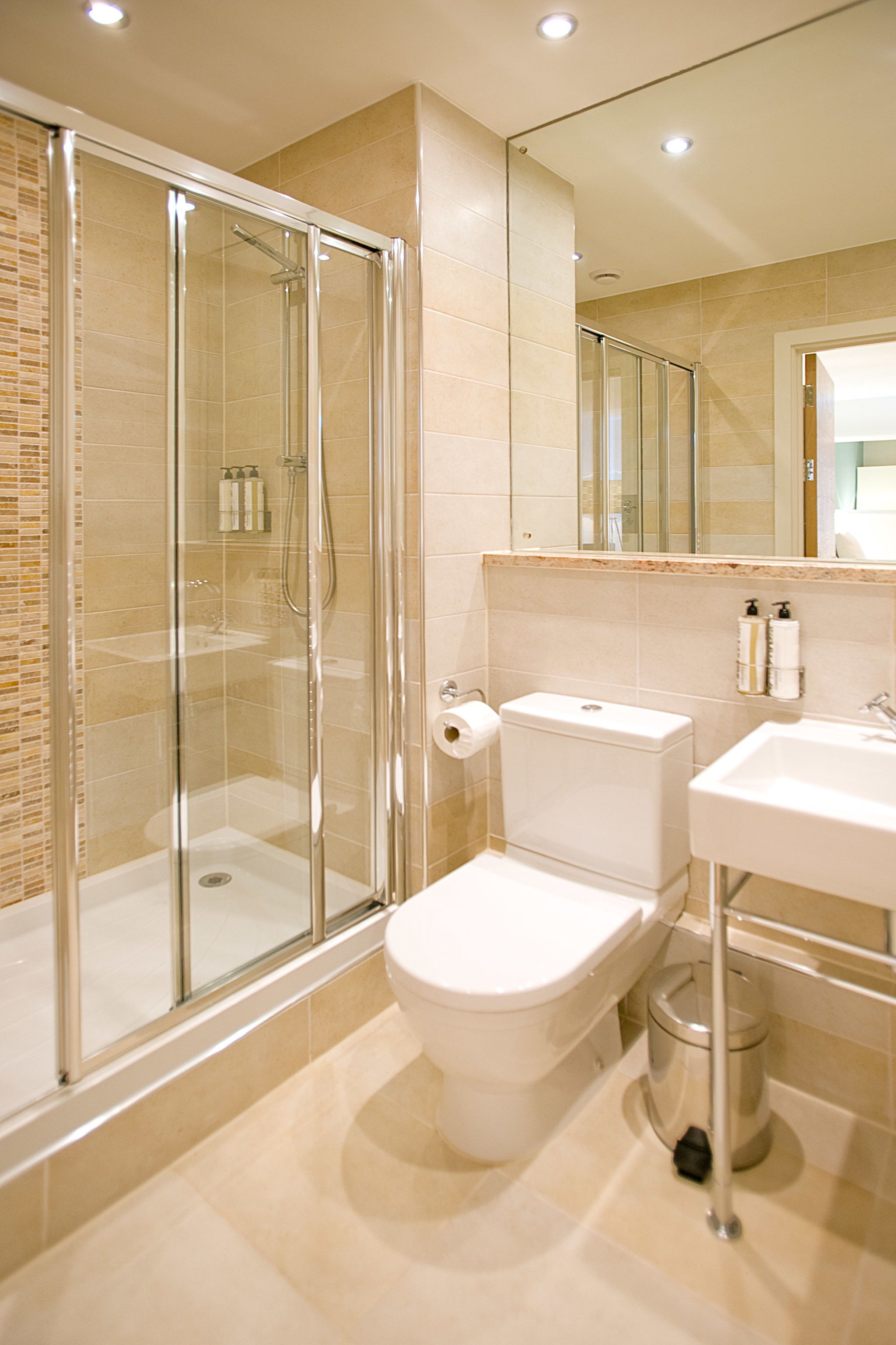 A modern bathroom with a glass-enclosed shower, a toilet, a sink, and a mirror.