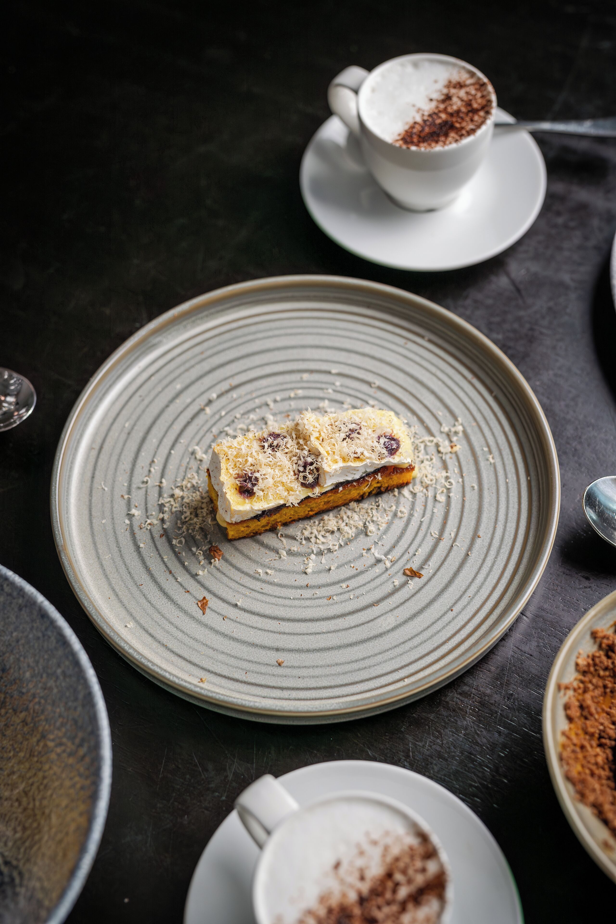 A dessert on a plate, a cup of coffee, and a bowl of what appears to be a dessert topping.