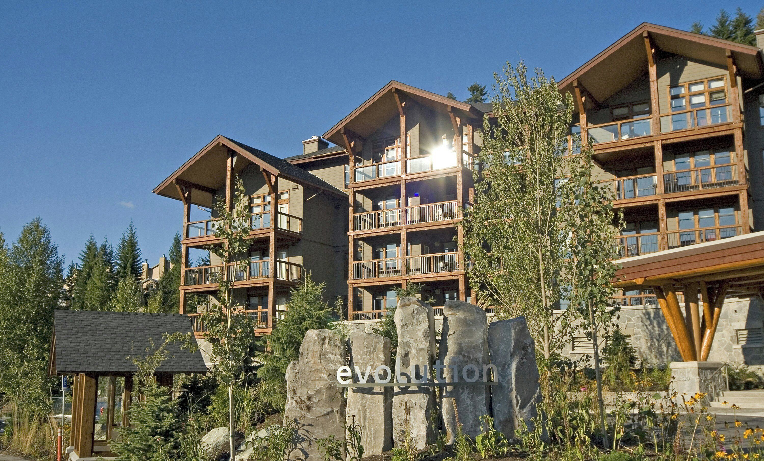 A multi-story lodge with balconies, surrounded by trees and a rock formation.
