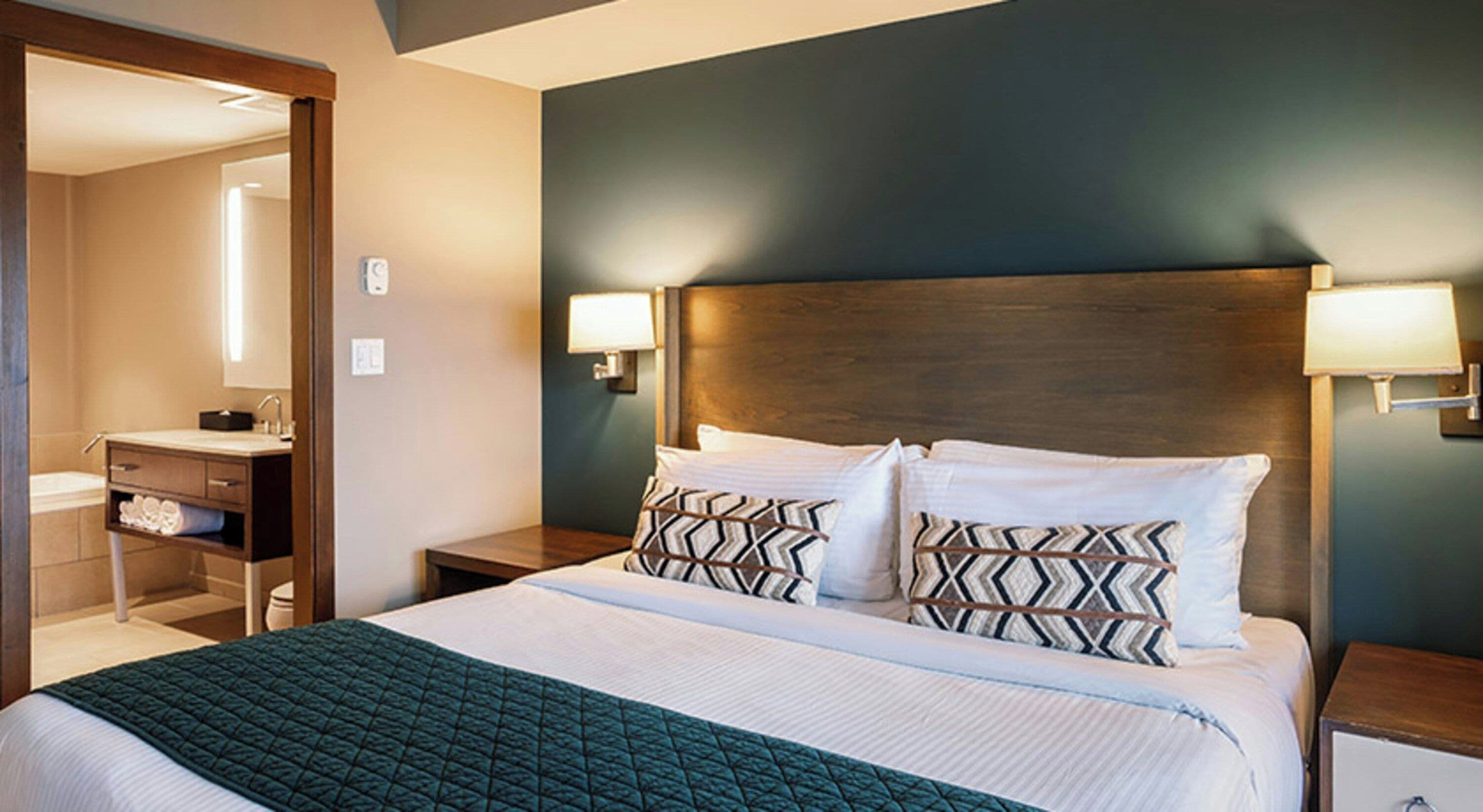 A hotel room with a large bed, two bedside tables, a nightstand, a wooden headboard, and a mirror.