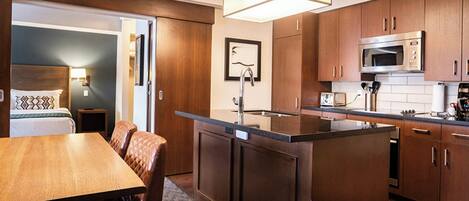 A compact hotel room with a kitchenette, a dining area, and a bed with a view.