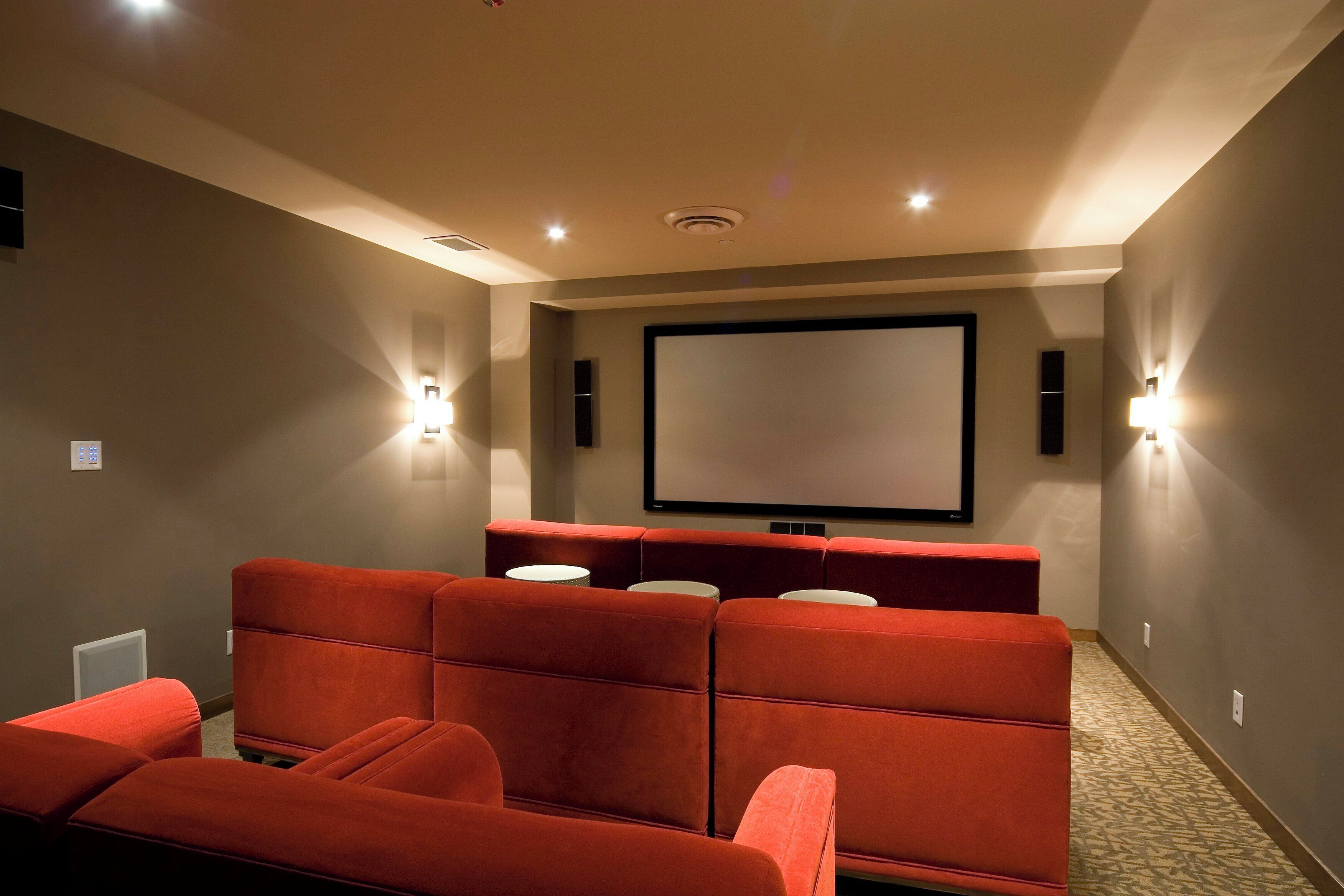 Ein Heimkino mit roten Sitzen, einer großen Leinwand und Wandlautsprechern.