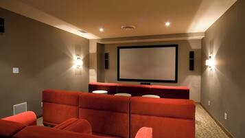 Ein Heimkino mit roten Sitzen, einer großen Leinwand und Wandlautsprechern.
