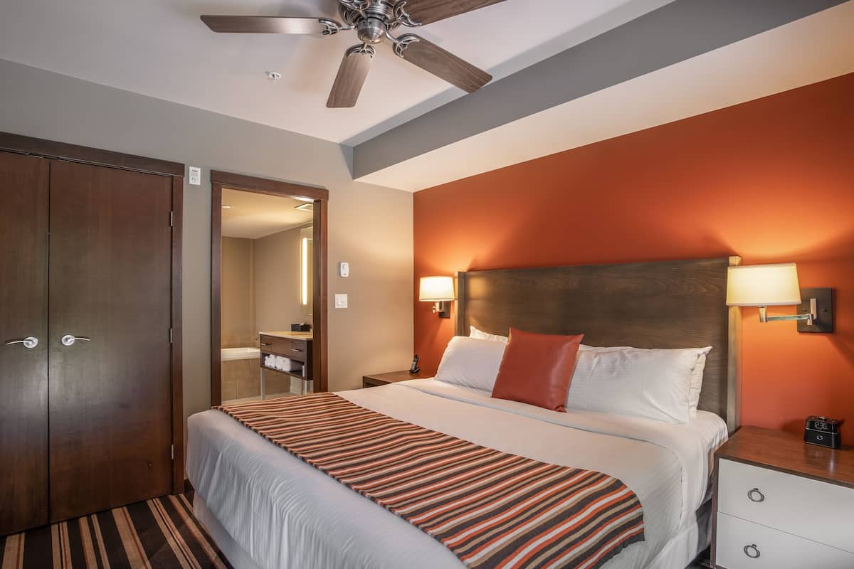 Habitación de hotel con cama, mesita de noche, lámpara y ventilador de techo.
