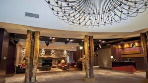 Un hall d’entrée agrémenté d’une cheminée en pierre, de piliers en bois et d’un lustre moderne.
