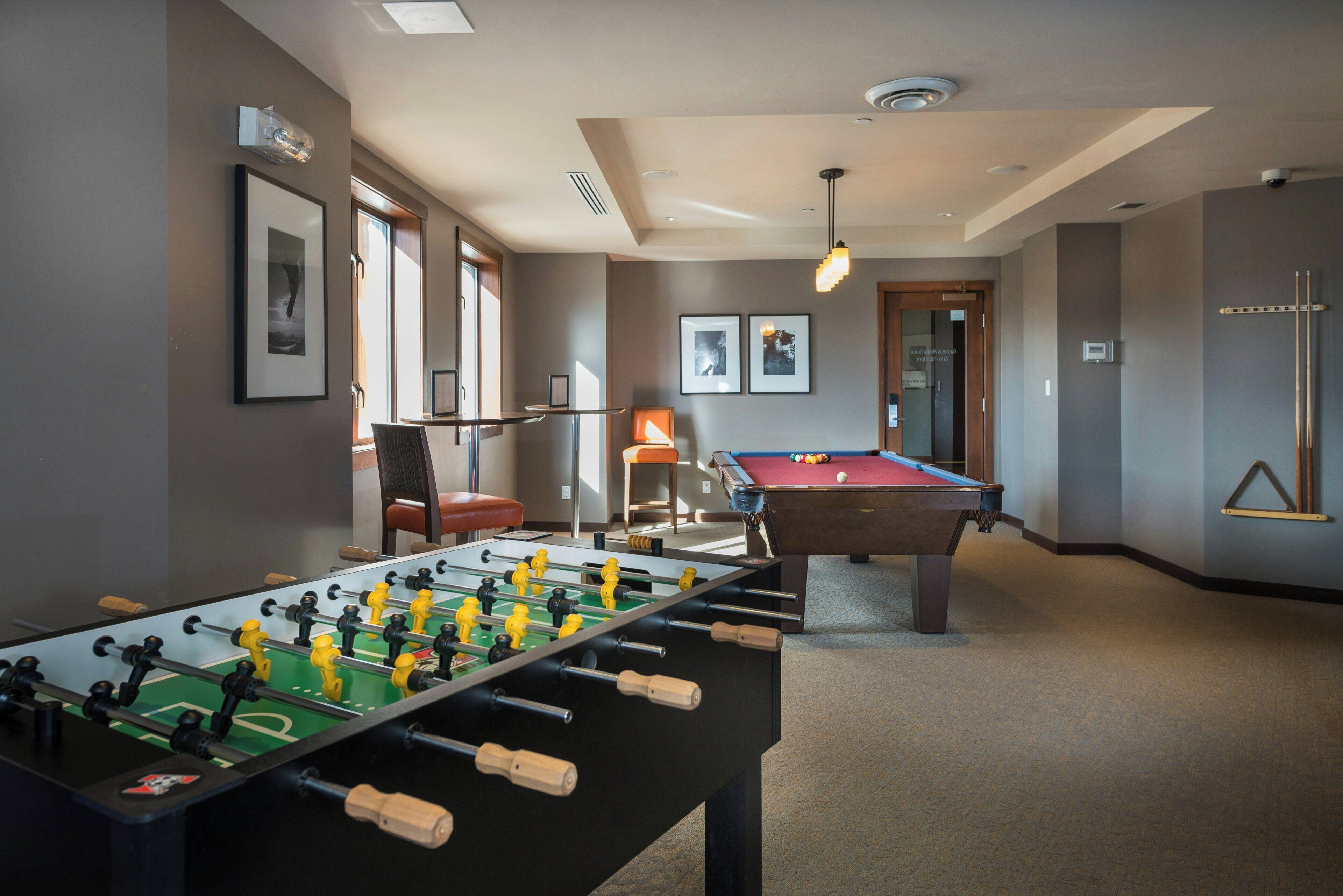 Une pièce avec un baby-foot, une table de billard et des tableaux encadrés accrochés aux murs.