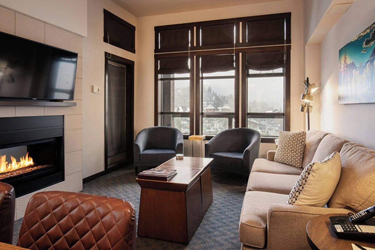 Una sala de estar moderna con chimenea, sillones de cuero, un sofá y un ventanal con vista a la ciudad.