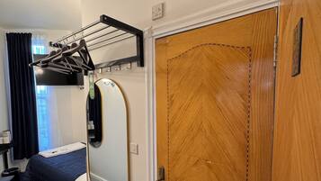 A hotel room with a bed, a built-in wardrobe, a mirror, and a clothes drying rack.