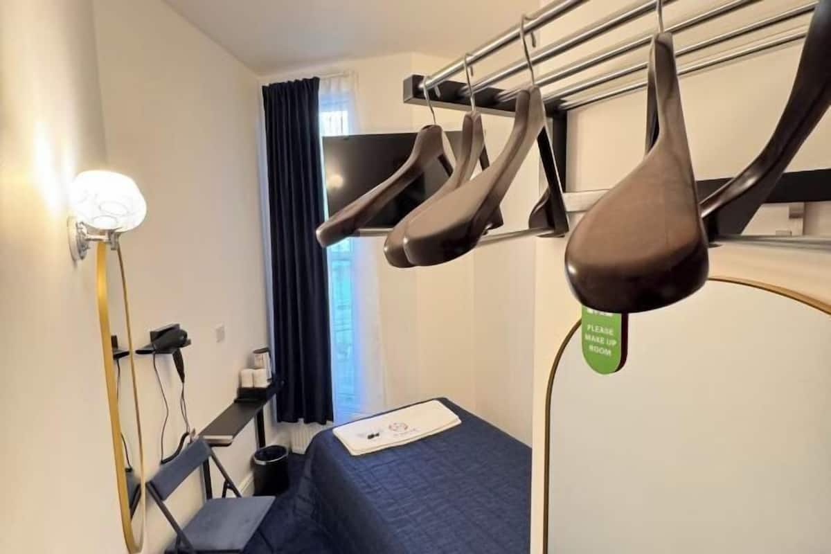 Una habitación de hotel con cama, televisión, escritorio con silla y zapatero.