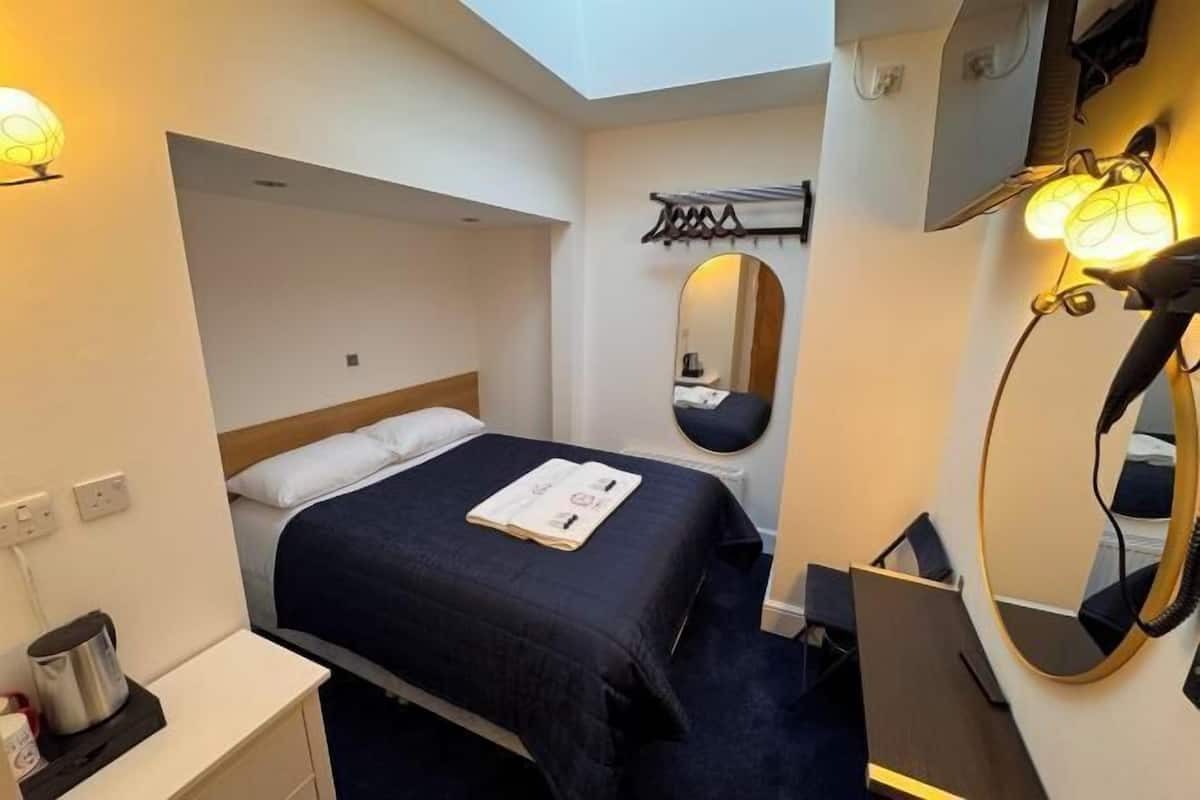 Una habitación de hotel con cama, mesita de noche, espejo y un pequeño escritorio con lámpara.