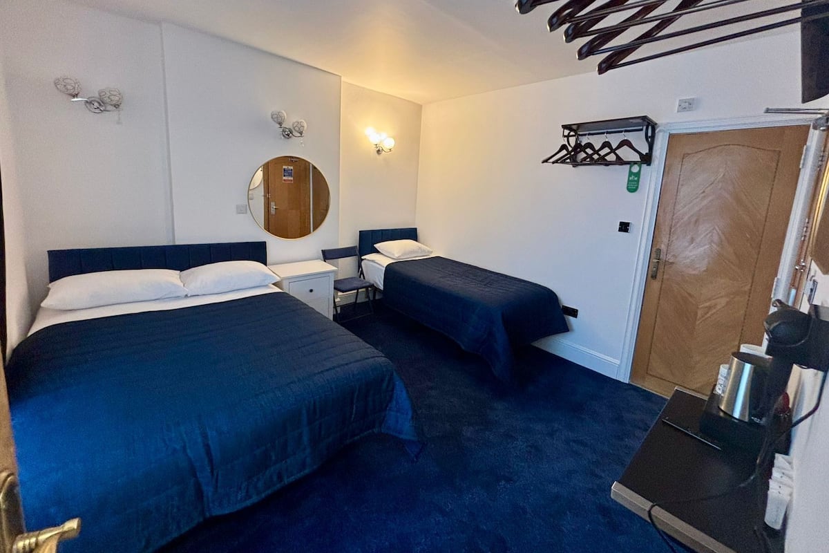 Habitación de hotel con dos camas, un espejo redondo, una lámpara de pared, un perchero y una puerta.