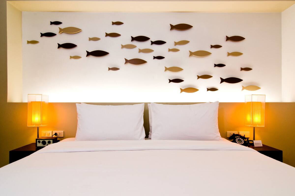 A hotel room with a bed, white bedding, two bedside lamps, and a wall with fish wall art.