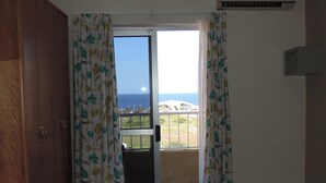 A room with a wooden wardrobe, a sliding glass door leading to a balcony with a view of the sea and buildings. - Qawra Point Holiday Complex (St. Paul's Bay)