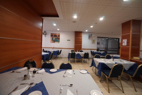 Un espace repas avec des tables disposées pour accueillir plusieurs personnes, des chaises et un ventilateur de plafond.