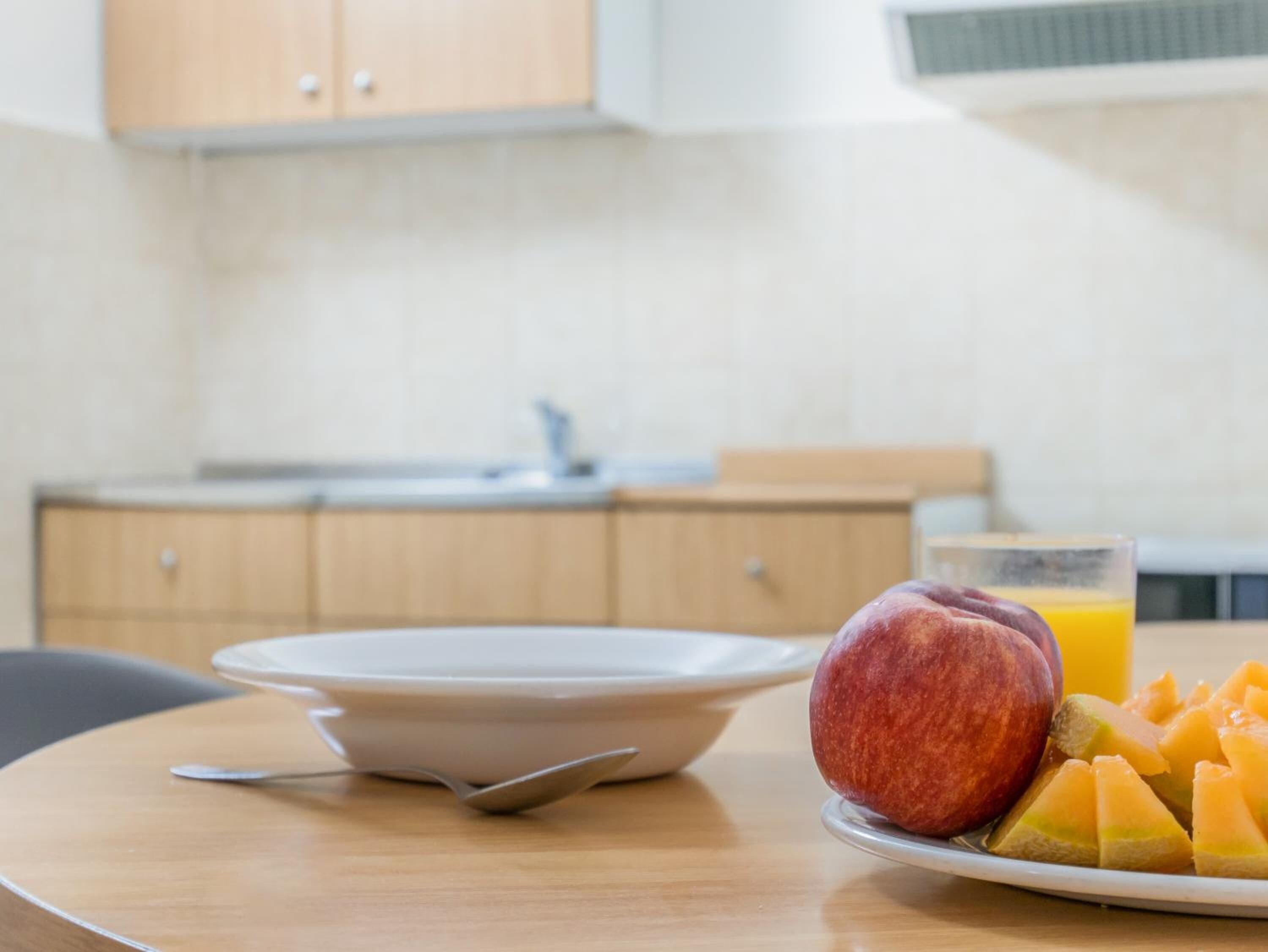 Una mesa de comedor con un tazón, un plato con fruta y un vaso de jugo de naranja.