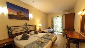 A hotel room with two beds, a dining table, a chair, a lamp, and a painting on the wall. - Qawra Point Holiday Complex (St. Paul's Bay)