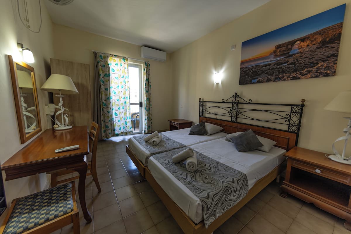 A hotel room with a bed, bedside tables, a desk with a chair, a mirror, and a window with curtains.