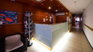 A reception area with a wooden reception desk, a glass partition, and a poster advertising tours and excursions. - Qawra Point Holiday Complex (St. Paul's Bay)